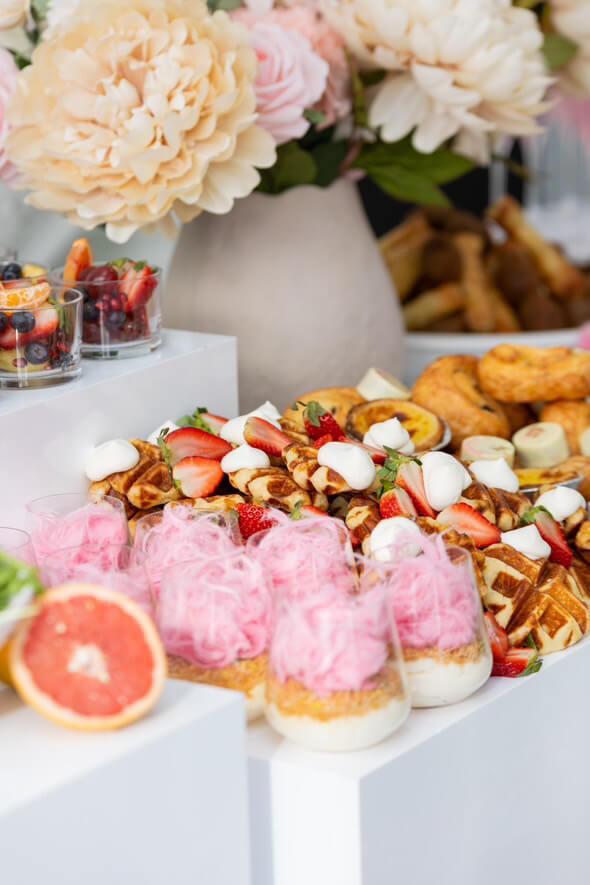 Brunch and dessert display with waffles, pastry cups, fruit, and florals