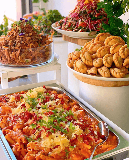Hot buffet detail with pasta, salads, and savory pastries on tiered serving dishes